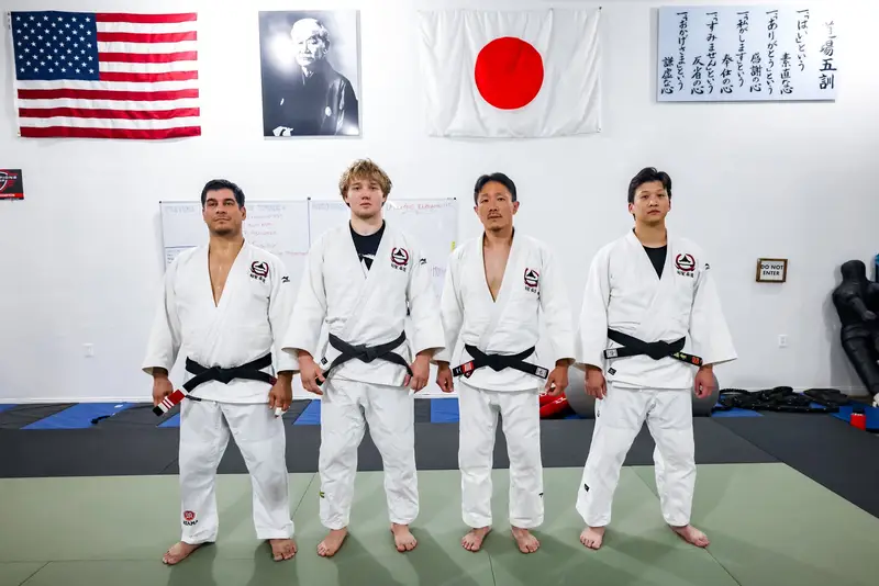 Kensei Judo black belts standing in the San Jose dojo in front of the U.S. and Japanese flags